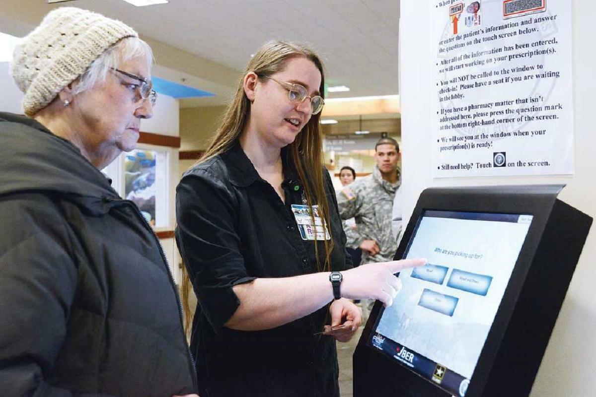 women is helping aged women for using self service kiosk at clinic